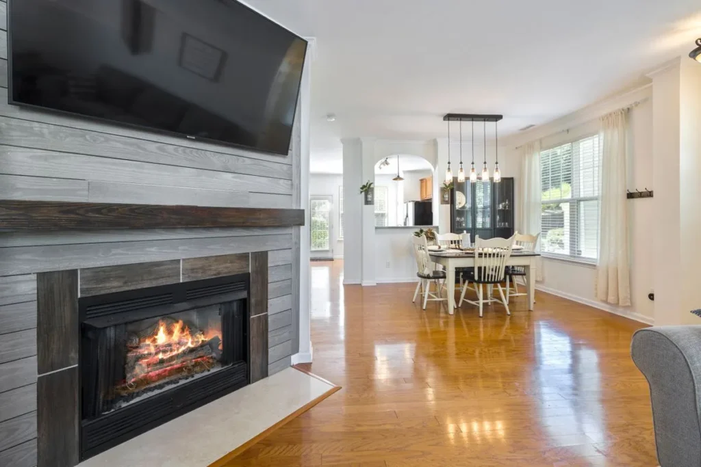 Fireplace insert with flames below a wall-mounted TV, with a dining area in the background