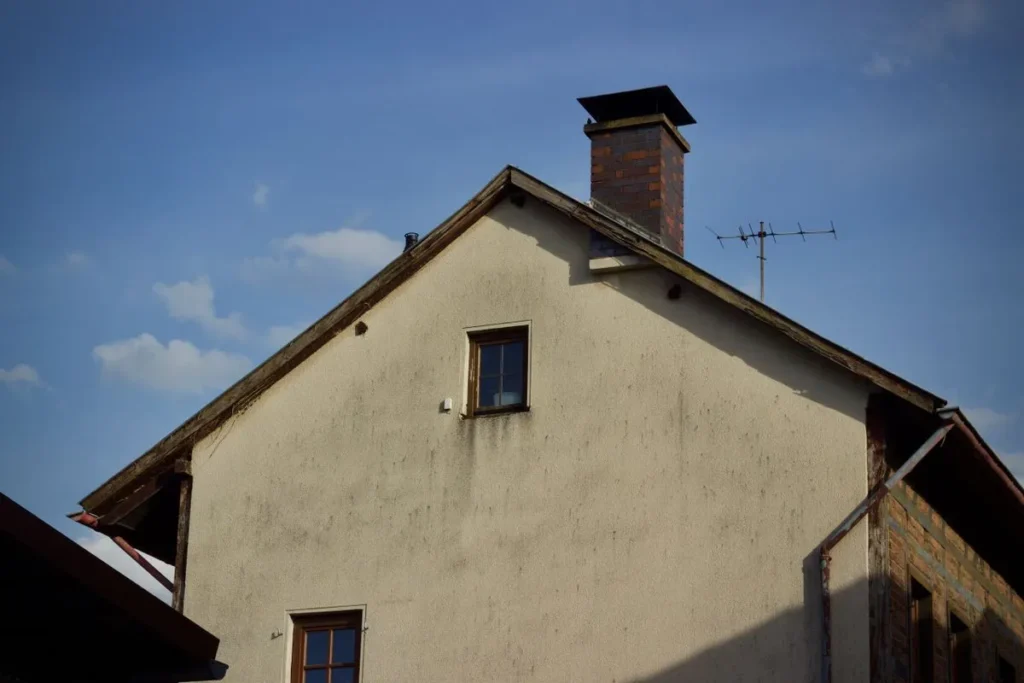 Stucco house gable with a brick chimney against a blue sky