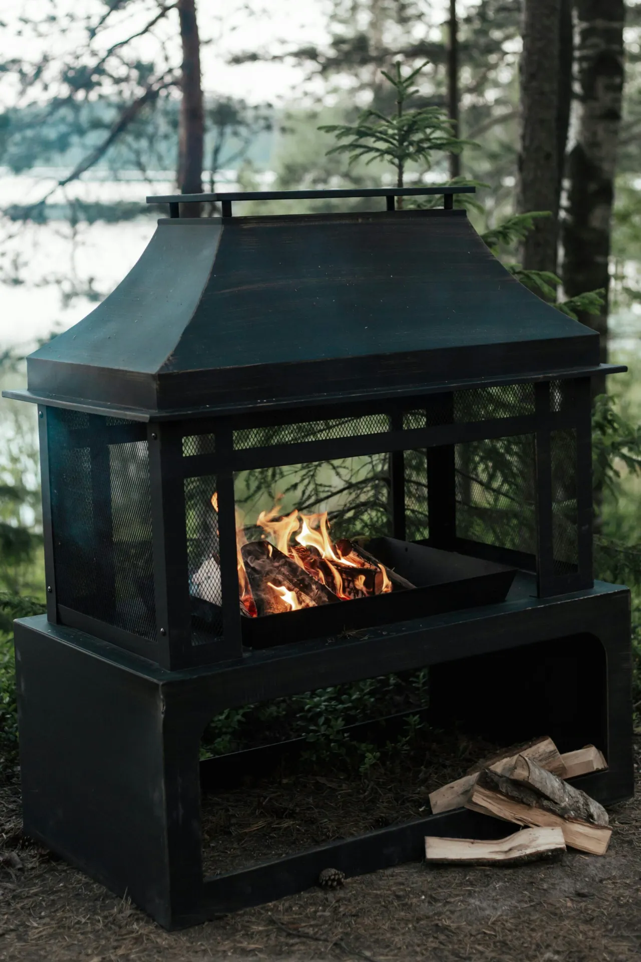 Black metal outdoor wood-burning fireplace with a chimney hood near a lake