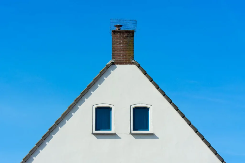 White house gable with a brick chimney and two small windows against a blue sky